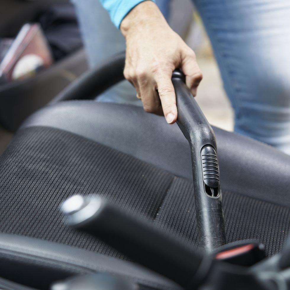 female hand holding the tube of the vacuum cleaner and cleaning the car seat